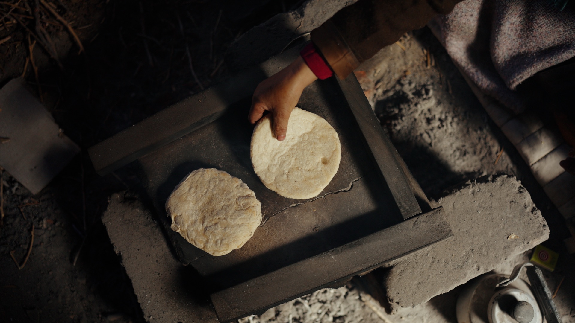 Hands placing traditional Ladakhi flatbread onto a stone oven over open flame