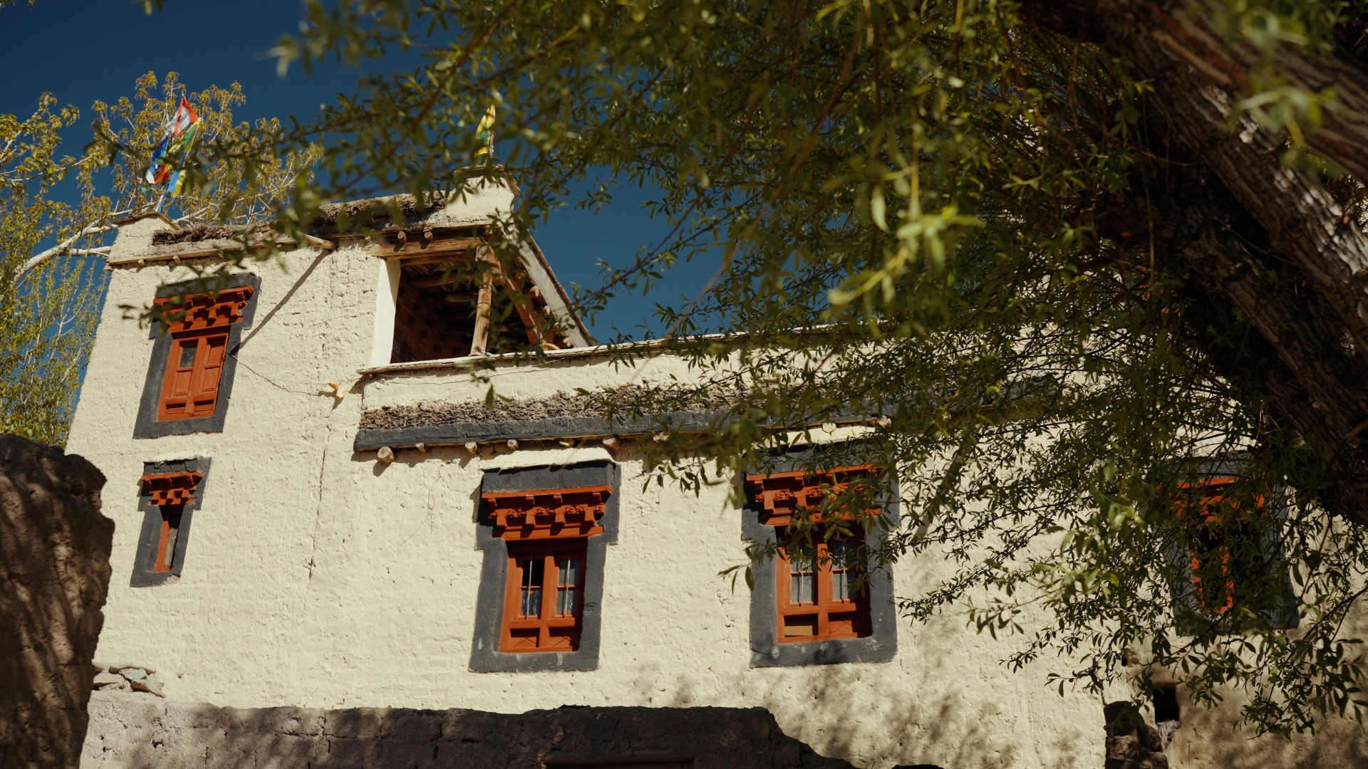 Traditional white-washed Ladakhi mud-brick house with decorated wooden windows and prayer flags