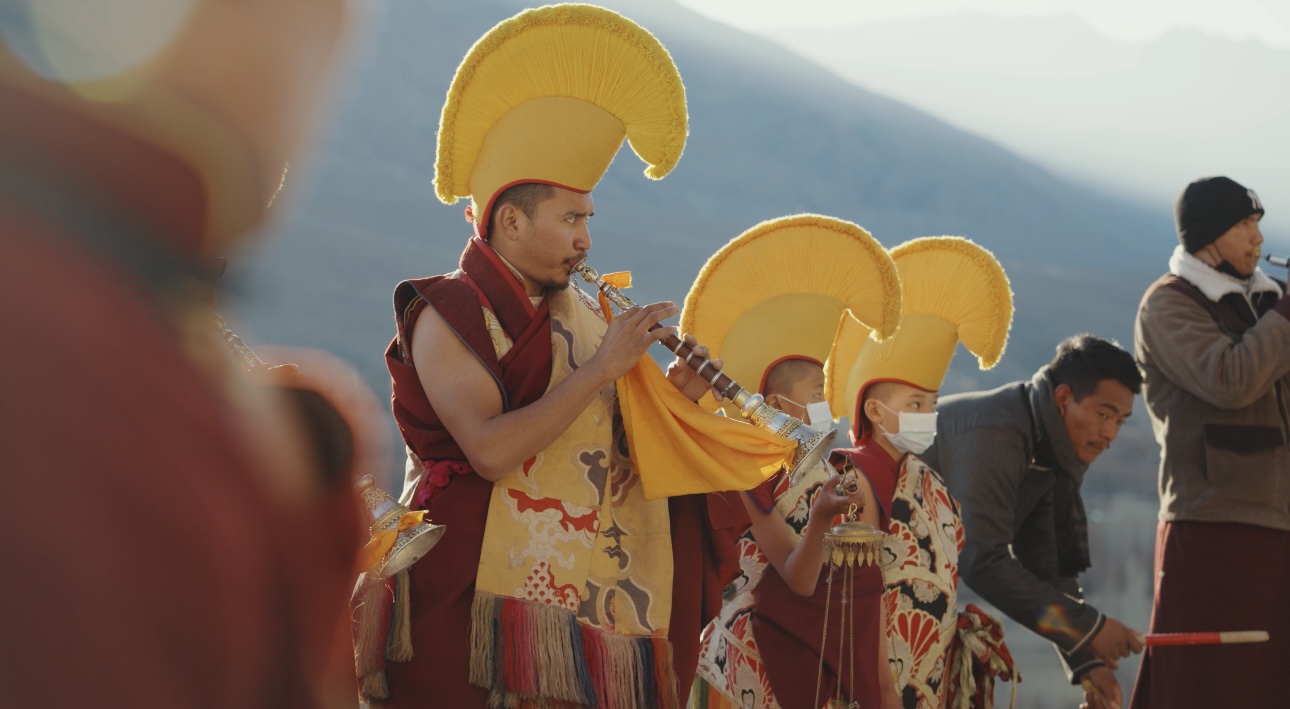 Buddhist monks in ceremonial robes playing instruments at a monastery festival