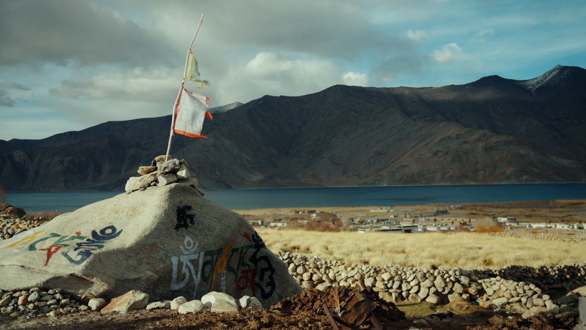 Prayer flags on a mani stone with Pangong Tso and mountain ranges behind