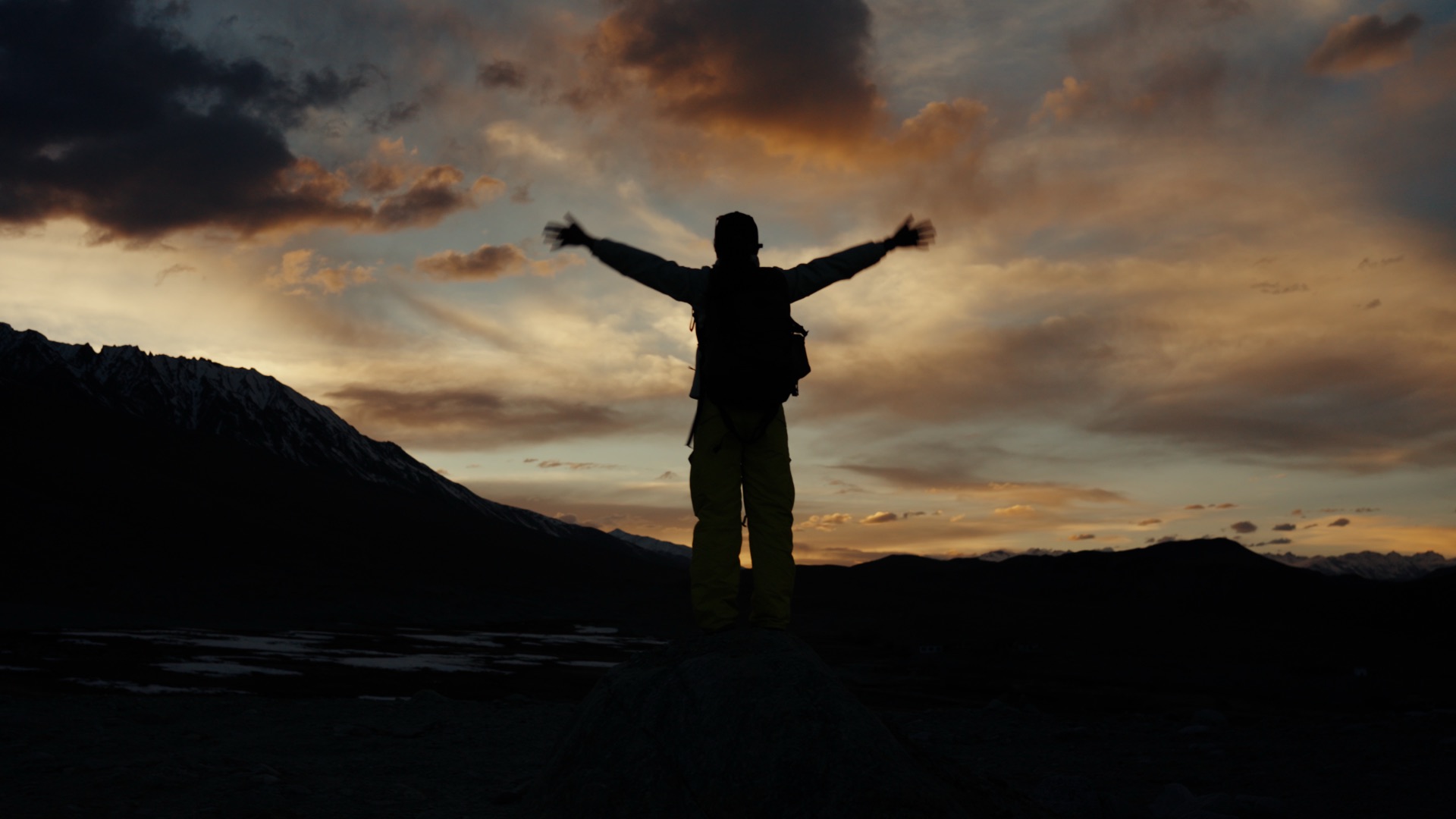 Silhouette of a hiker with arms wide open at a mountain summit against a fiery sunset sky