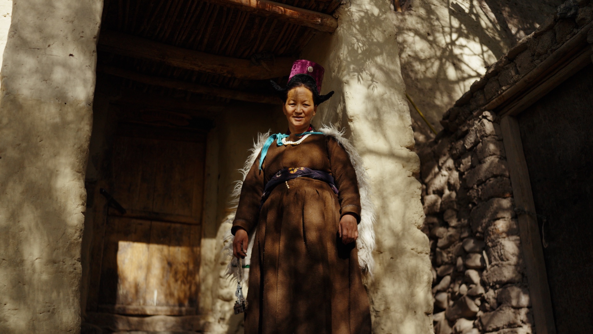 Ladakhi woman in traditional goncha and perak headdress standing in a village doorway