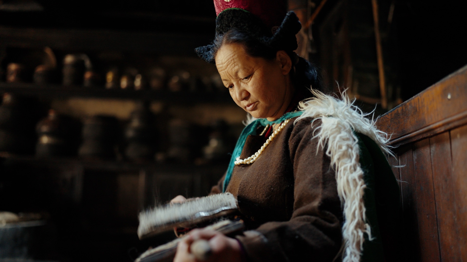 Ladakhi woman in traditional dress combing pashmina wool by warm light