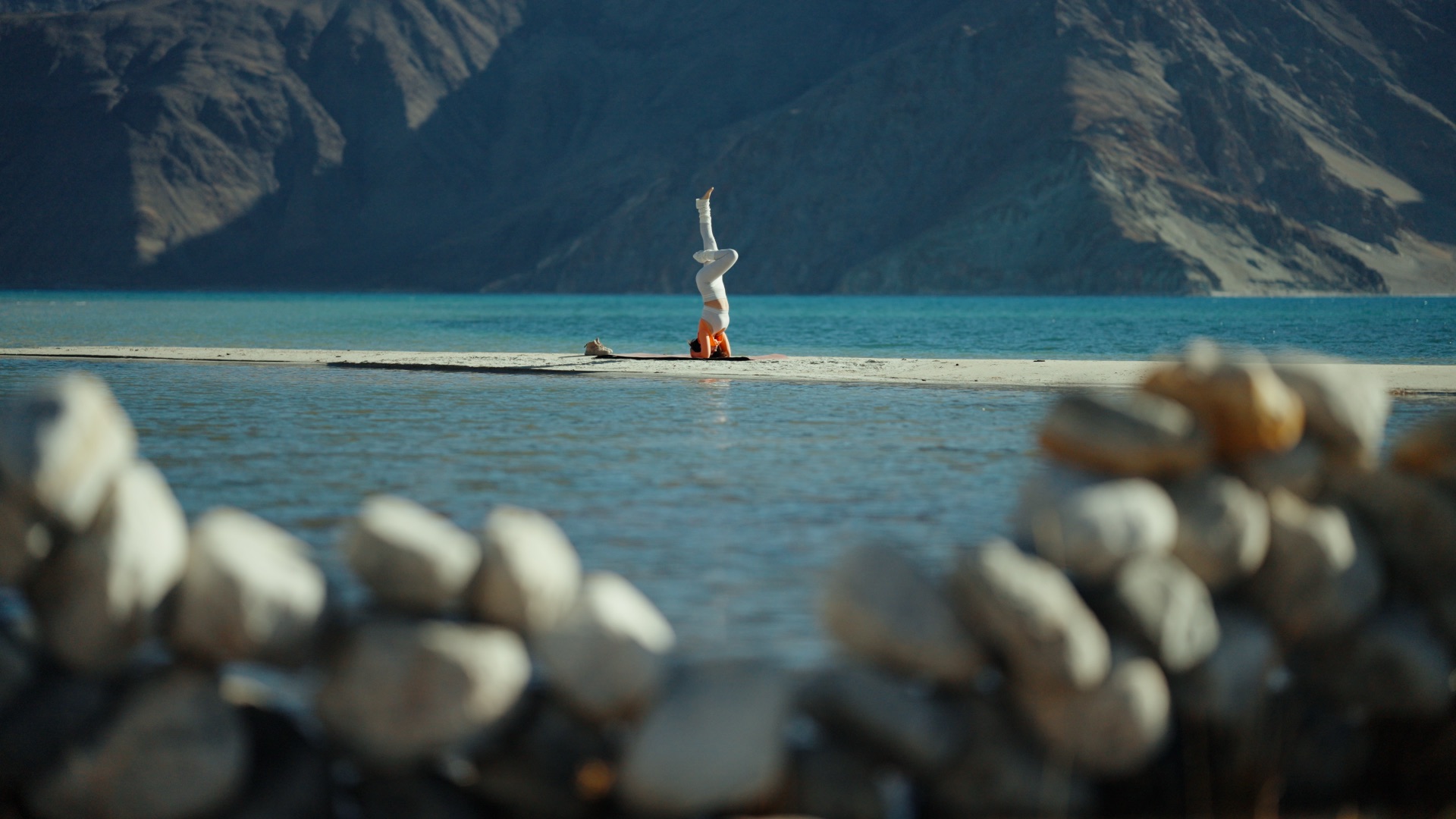Yoga headstand at the shore of Pangong Tso with stone cairns in the foreground