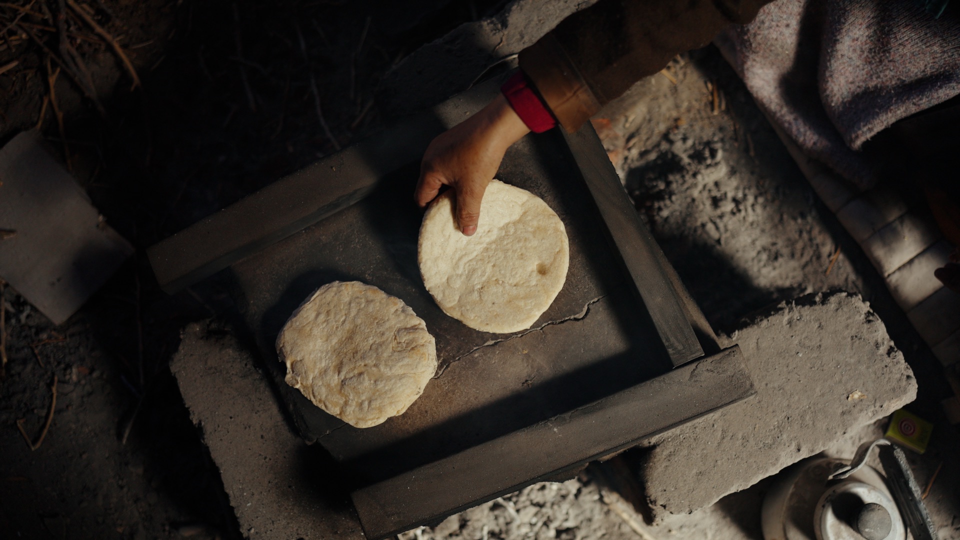 Hands placing traditional Ladakhi flatbread onto a stone oven over open flame