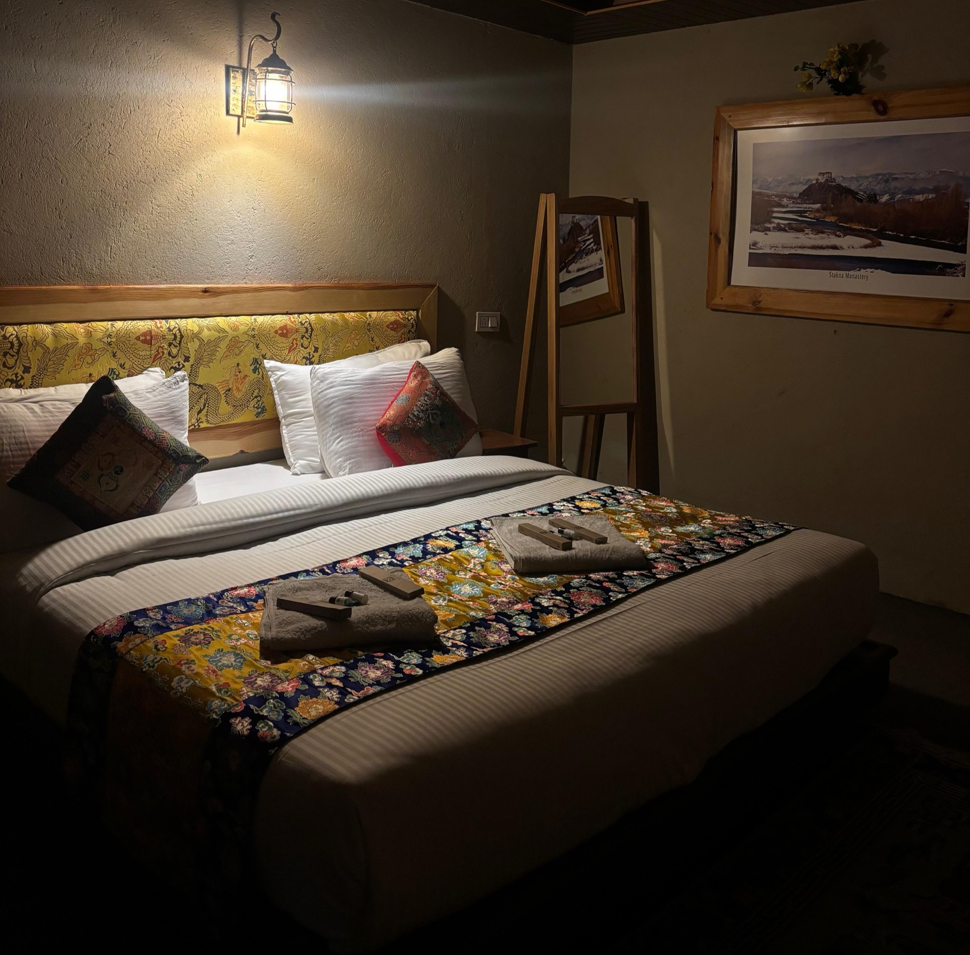 Warmly lit hotel room with Ladakhi textile bed runner and traditional wall lamp